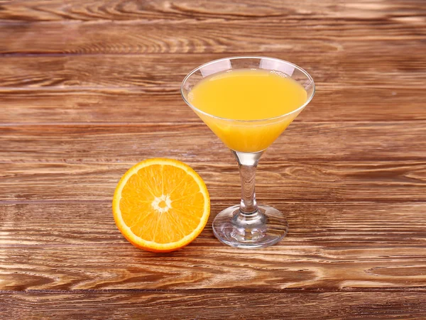 Glass of freshly pressed orange juice with sliced orange half on wooden table