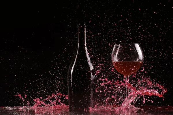 Bottle with red wine, water splash, wine on table on black background, big splash around bottle of red wine