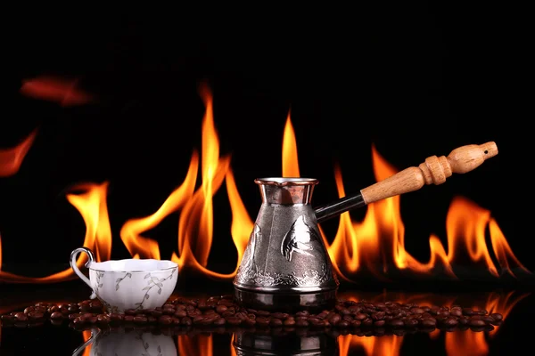 Fired cup of coffee with coffee beans and turk on black background