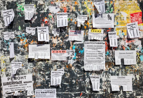 Dirty bulletin board filled with paper notices on russian language