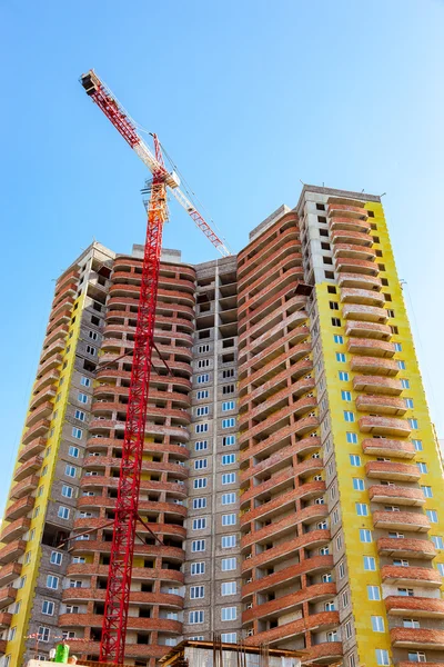 New tall apartment building under construction with crane against blue sky background
