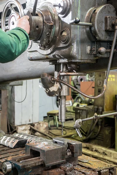 Machinist working on industrial drilling machine in workshop