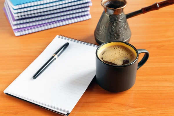 Cup of coffee on the office desk with notebook and pen