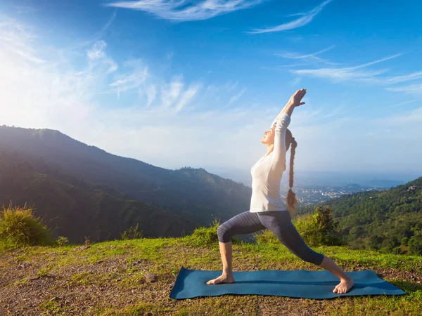 Woman doing yoga asana Virabhadrasana 1 - Warrior pose outdoors