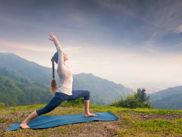 Woman doing yoga asana Virabhadrasana 1 - Warrior pose outdoors
