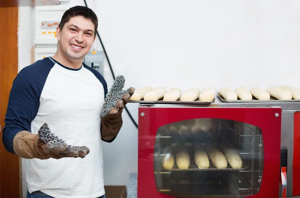 Smiling glad handsome man baking baguettes