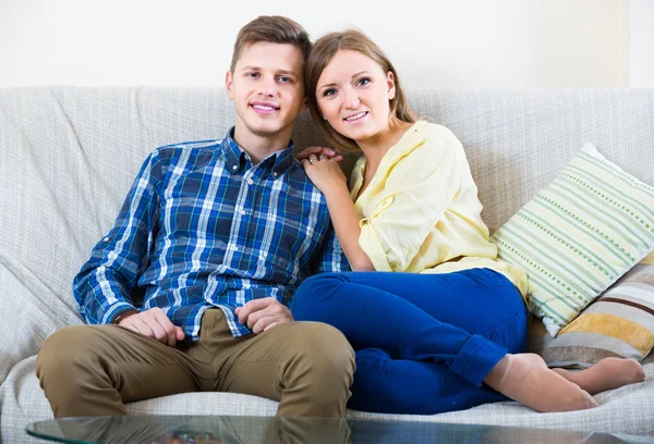 Guy and pretty girl cuddling on sofa indoors