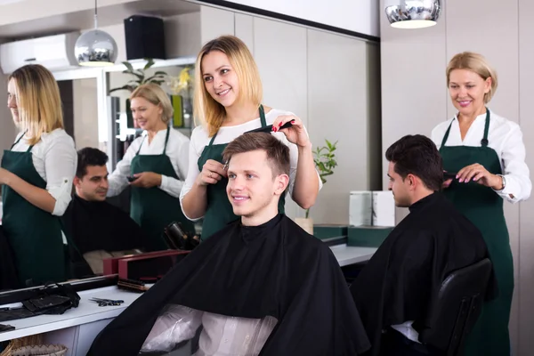 Positive blonde hairdresser serving teenager