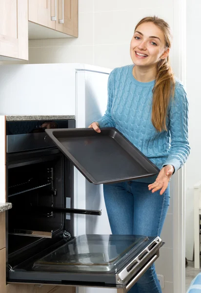 Woman placing roasting tray in kitchen oven