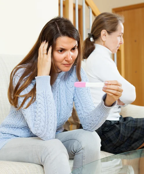 Girl with pregnancy test against unhappy mature mother