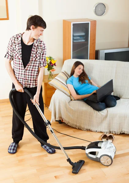 Man cleaning  while wife lying with notebook