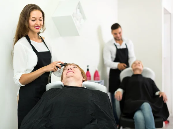 Hairdresser washing head of adult woman