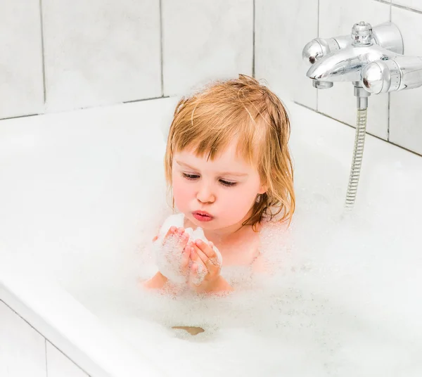 Cute two year old baby bathes in a bath with foam