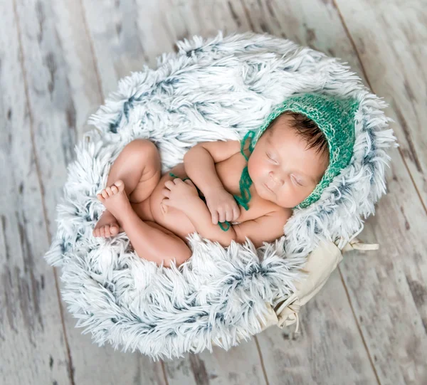 Newborn baby with green hat sleeping in a basket