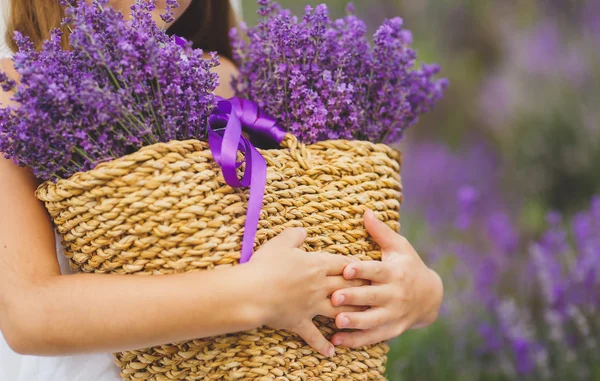 Happy little girl is in a lavender field holds a basket of flowers