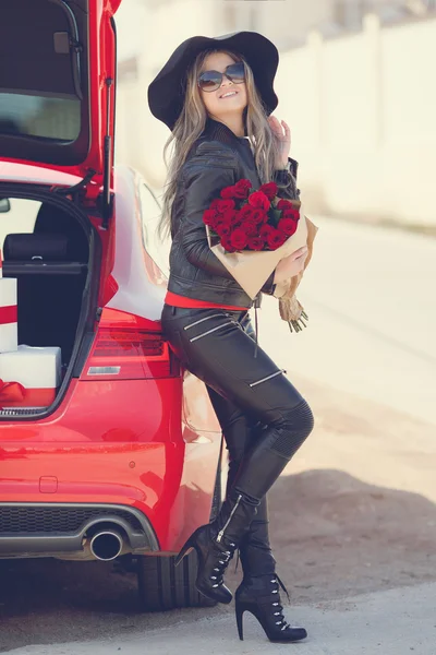Stylish blonde with a bouquet of red roses near the car