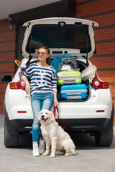 Woman with dog by car full of suitcases.
