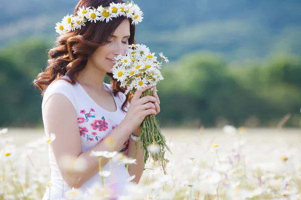 A pregnant woman in a field with a bouquet of white daisies