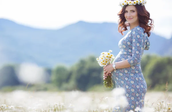 Pregnant woman in field with basket of white daisies