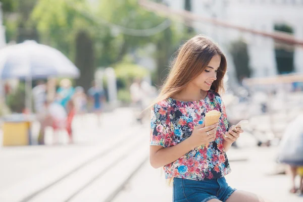 Beautiful girl with ice cream reads message on mobile phone