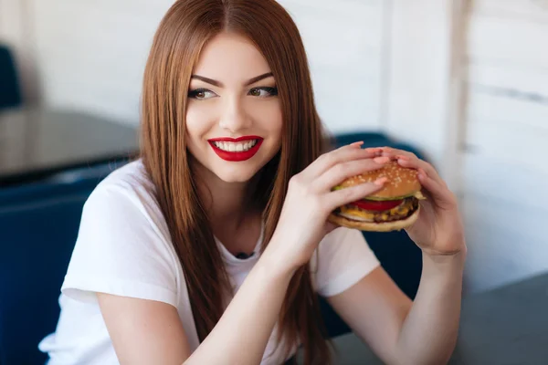 Lady with a hamburger for a table in a cafe