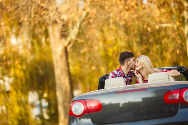 Loving couple in a black convertible in the autumn park.