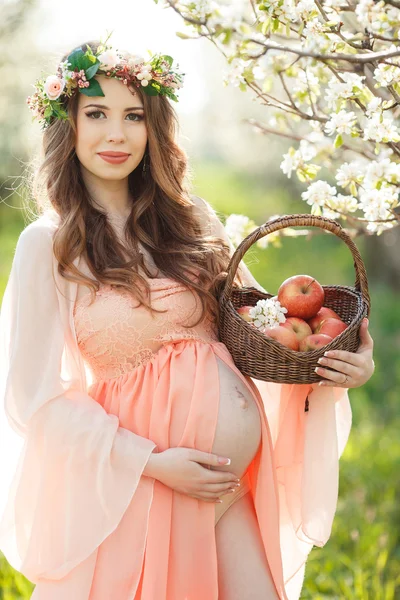 Pregnant woman in the spring garden with a basket of ripe apples.