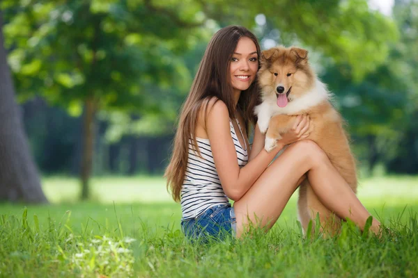 Young beautiful woman playing in a green park with a small puppy collie