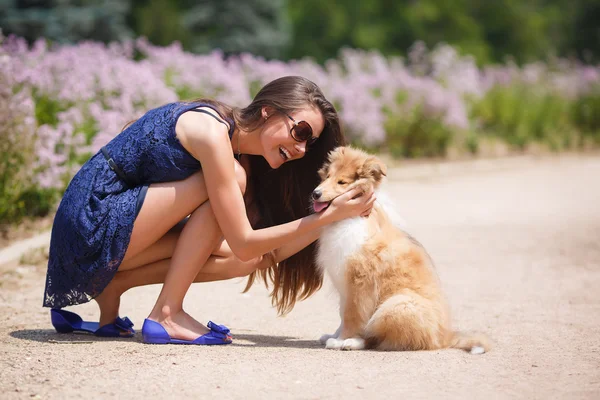 Young beautiful woman playing in a green park with a small puppy collie
