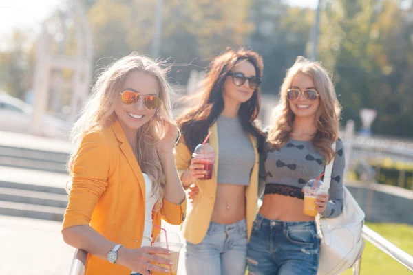 Three girls are walking in the Park in summer and drink fruit juice