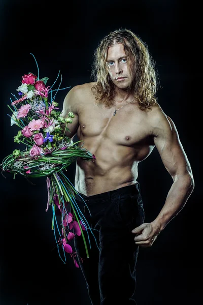 Male fitness model shirtless holding a bouquet of flowers
