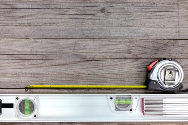 Spirit level with tape measure on gray wooden background