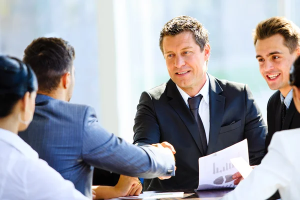 Business colleagues sitting at a table during a meeting with two male executives shaking hands