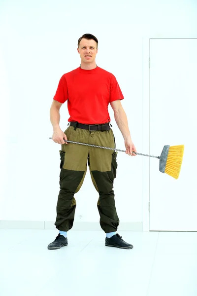 Full length portrait of a cleaner in a uniform with a broom isolated white background