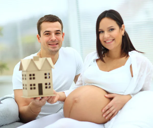 Man and pregnant woman are holding the model of the future home