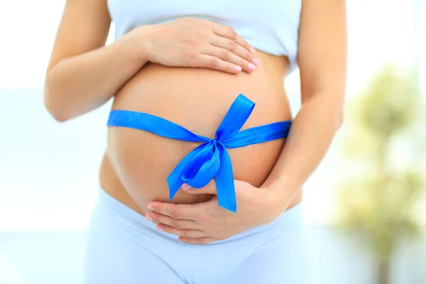 Woman holding hands on her baby bump, tied with a blue bow