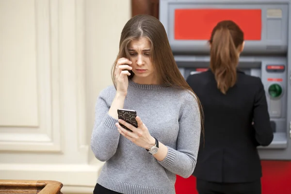 Frustrated young woman stands on against ATM