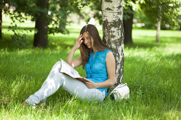 Happy woman leafing through a magazine while sitting in the summ