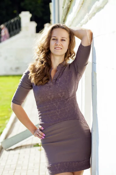 Beautiful young woman in sexy brown dress, against white wall