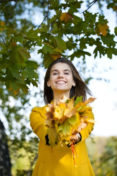Happy young woman in yellow coat in autumn park