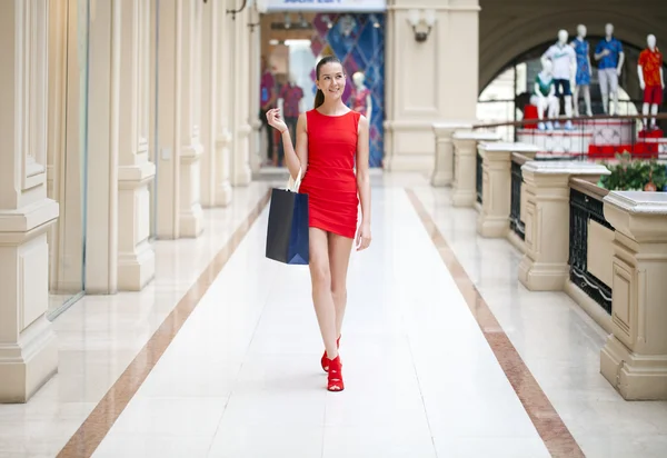 Beautiful smiling girl in a red dress, holding shopping bags