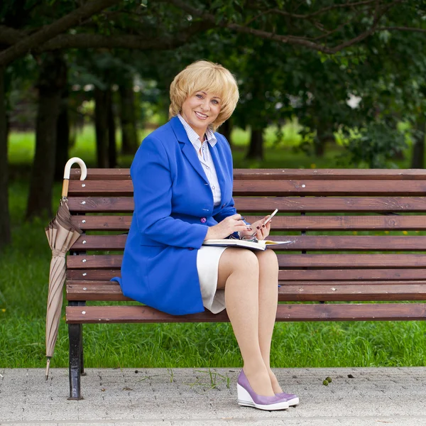 Mature business woman in a jacket with diary sitting on a bench