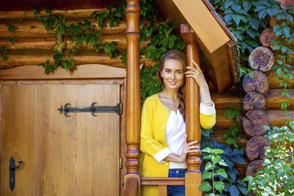 Happy young woman standing on the porch of a wooden house