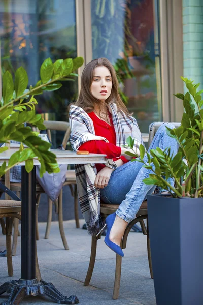 Young beautiful girl sits in summer cafe in the street wrapped b