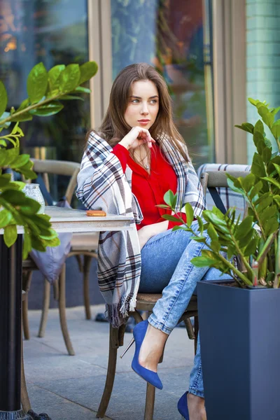 Young beautiful girl sits in summer cafe in the street wrapped b