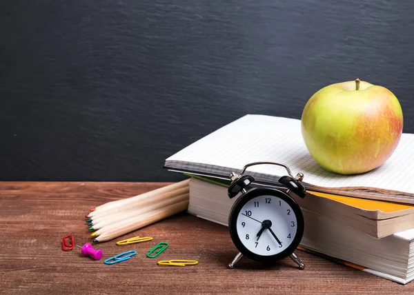 Books, apple and clock on the wooden table.