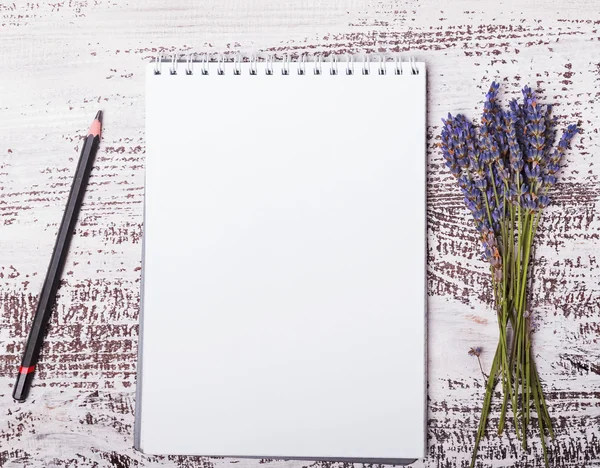 Empty notepad, pensil and lavender flowers on the whitw wooden b