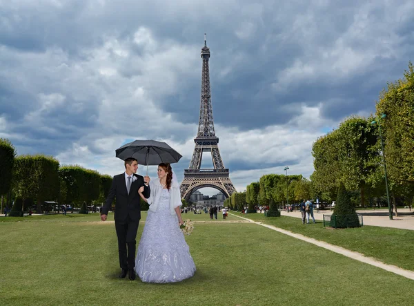 Beautiful wedding couple in Paris. Bride and groom walking under an umbrella on a rainy day on Champ de Mars in front of the Eiffel Tower