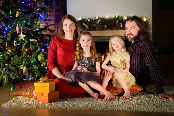 Young happy family of four sitting by a fireplace on Christmas eve