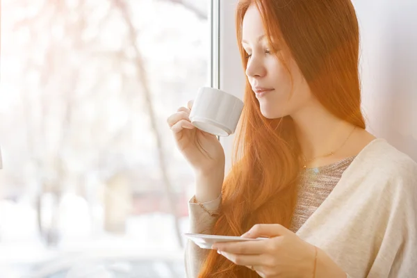 Beautiful young woman with a cup of morning coffee by the window.
